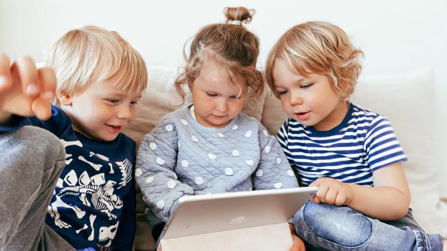 
		Drei Kinder schauen in ein Tablet
	