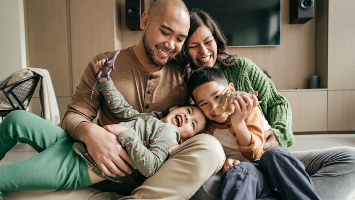 Eltern mit zwei Kindern sitzen lachend zusammen im Wohnzimmer auf dem Boden